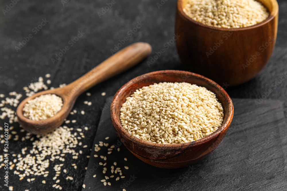 Wooden bowl of sesame seeds on dark background, closeup Wooden bowl of sesame seeds on dark background, closeup