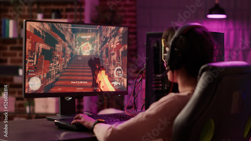 Fotografie Over shoulder view of gamer girl using pc gaming setup relaxing playing multiplayer online action video game talking using headset
