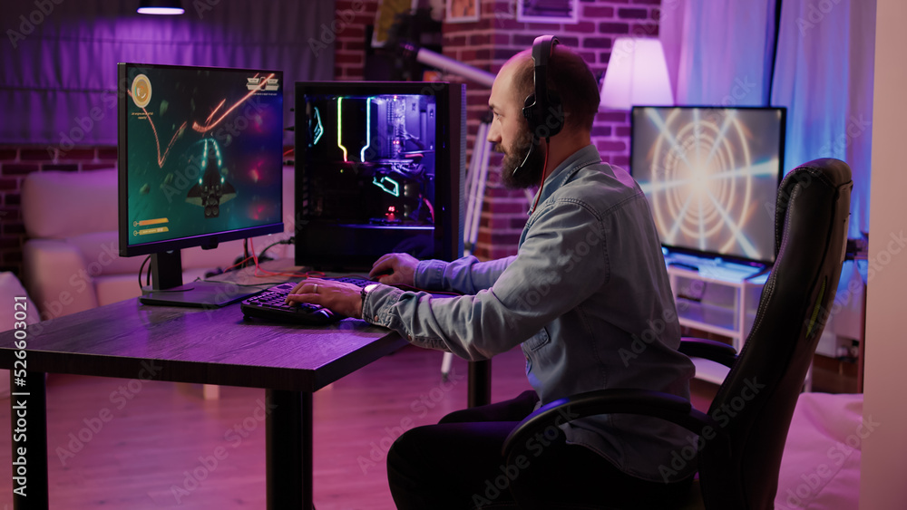 Gamer playing fast paced space shooter simulation screaming victorious at the computer screen after winning difficult level. Caucasian man celebrating victory in internet multiplayer action game. Gamer playing fast paced space shooter simulation screaming victorious at the computer screen after winning difficult level. Caucasian man celebrating victory in internet multiplayer action game.