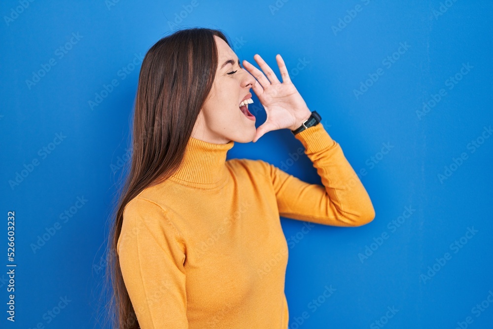 Young brunette woman standing over blue background shouting and screaming loud to side with hand on mouth. communication concept. Young brunette woman standing over blue background shouting and screaming loud to side with hand on mouth. communication concept.