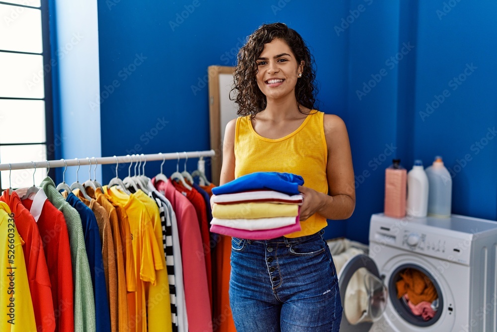 Young latin woman smiling confident holding folded clothes at laundry room Young latin woman smiling confident holding folded clothes at laundry room