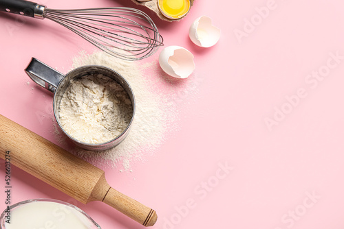 Mug with flour  whisk and rolling pin on pink background