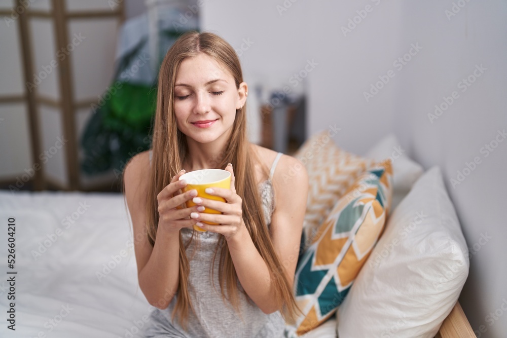 Young caucasian woman drinking cup of coffee sitting on bed at bedroom Young caucasian woman drinking cup of coffee sitting on bed at bedroom