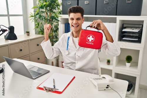 Young hispanic doctor man holding first aid kit screaming proud  celebrating victory and success very excited with raised arm