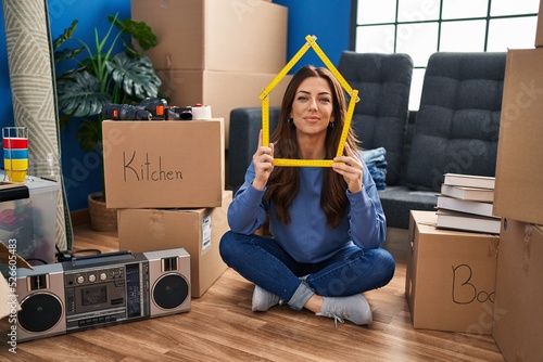 Young brunette woman sitting on the floor at new home smiling with a happy and cool smile on face. showing teeth. photo