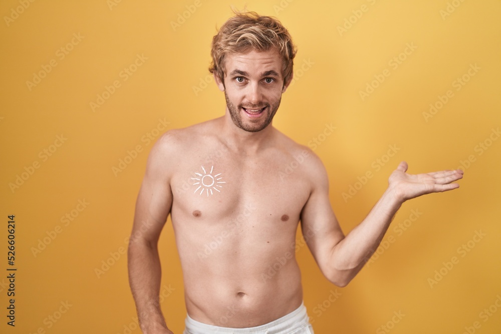 Caucasian man standing shirtless wearing sun screen smiling cheerful presenting and pointing with palm of hand looking at the camera.