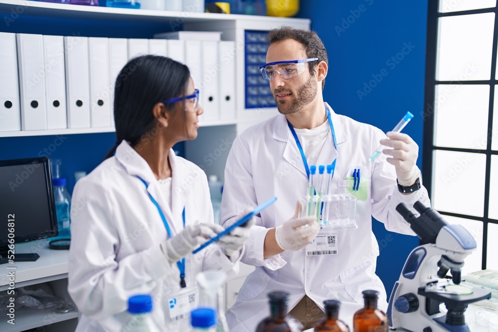 Man and woman scientists using touchpad holding test tubes at laboratory