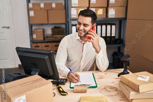 Young hispanic man e-commerce business worker talking on the smartphone at office