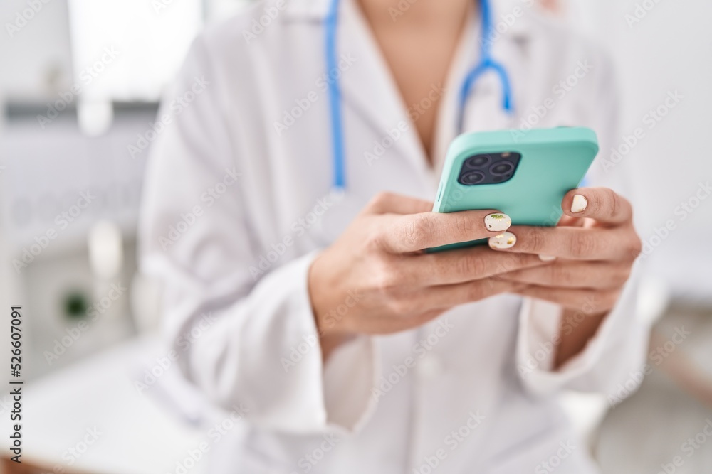 Young beautiful hispanic woman doctor using smartphone at clinic Young beautiful hispanic woman doctor using smartphone at clinic
