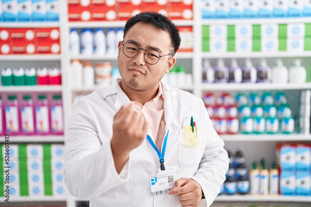 Chinese young man working at pharmacy drugstore beckoning come here gesture with hand inviting welcoming happy and smiling Chinese young man working at pharmacy drugstore beckoning come here gesture with hand inviting welcoming happy and smiling