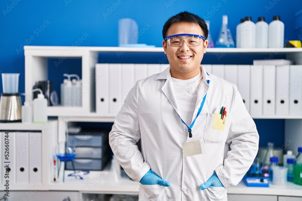 Young chinese man wearing scientist uniform standing at laboratory