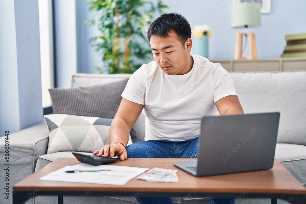 Young chinese man accounting economy using laptop and calculator at home Young chinese man accounting economy using laptop and calculator at home