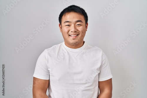 Young chinese man standing over white background with a happy and cool smile on face. lucky person.