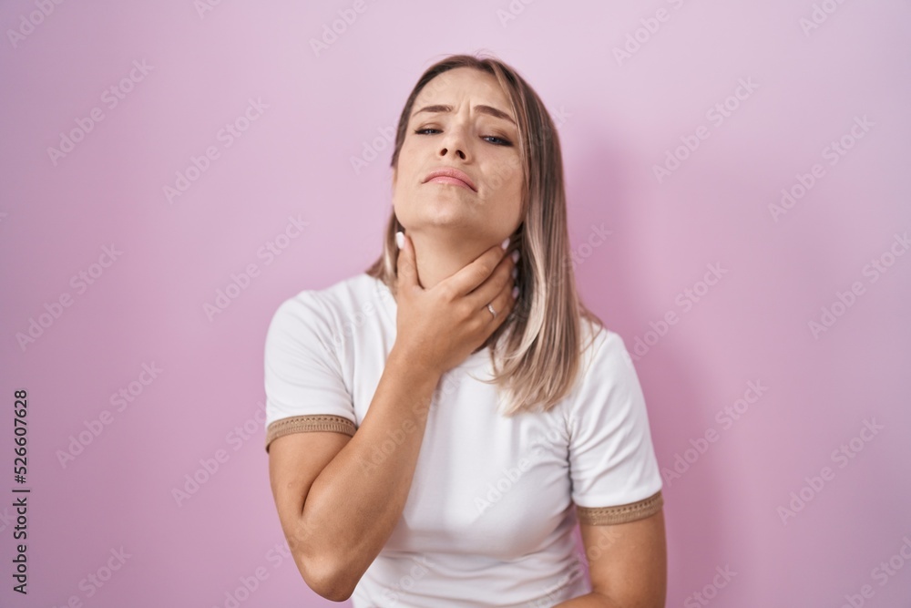 Blonde caucasian woman standing over pink background touching painful neck, sore throat for flu, clod and infection Blonde caucasian woman standing over pink background touching painful neck, sore throat for flu, clod and infection