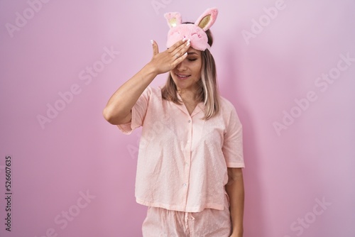 Blonde caucasian woman wearing sleep mask and pajama surprised with hand on head for mistake, remember error. forgot, bad memory concept.