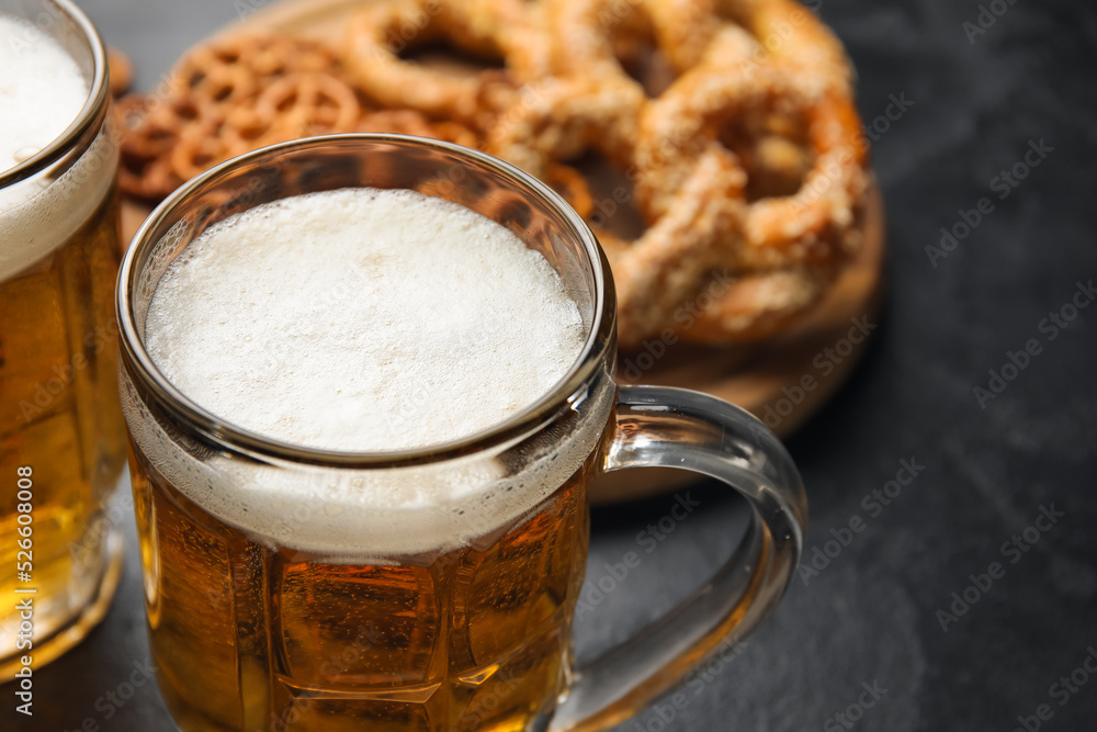 Mugs of fresh beer and pretzels on dark background, closeup. Oktoberfest celebration Mugs of fresh beer and pretzels on dark background, closeup. Oktoberfest celebration
