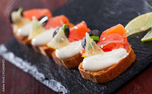 Fototapeta Naklejka Na Ścianę i Meble -  Canapes on toasted bread with smoked salmon, olives and creamy sauce on black serving board..