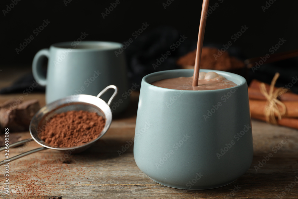 Pouring hot cocoa drink into cup on wooden table Pouring hot cocoa drink into cup on wooden table