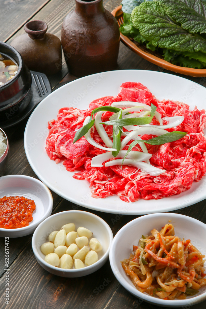 Bulgogi, a traditional Korean food on a black stone plate with a wooden background, and side dishes 나무배경에 검은 돌판위에 있는 한국 전통 음식인 불고기와 밑반찬 Bulgogi, a traditional Korean food on a black stone plate with a wooden background, and side dishes 나무배경에 검은 돌판위에 있는 한국 전통 음식인 불고기와 밑반찬