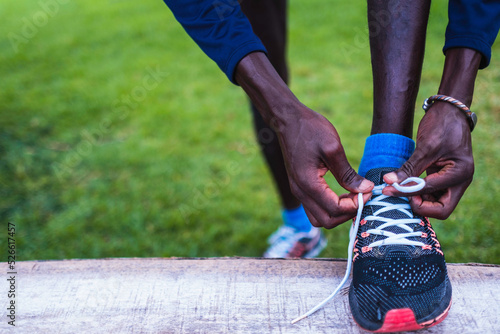 black man in sportswear, laces up his sneakers to start running.