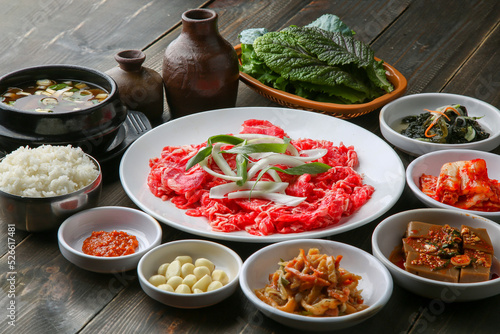 Bulgogi, a traditional Korean food on a black stone plate with a wooden background, and side dishes 나무배경에 검은 돌판위에 있는 한국 전통 음식인 불고기와 밑반찬