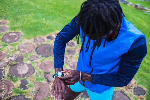 Black man in sportswear manipulating his watch before starting to run.