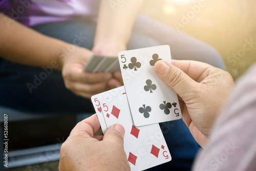 Paper cards number 5 holding in hands of woman who sitting and playing card with friend, soft and selective focus, freetimes and hobby activity at home concept.