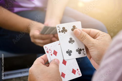Paper cards number 5 holding in hands of woman who sitting and playing card with friend, soft and selective focus, freetimes and hobby activity at home concept.