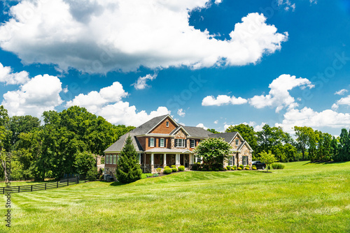 Large country white house and summer landscape with a perfect lawn. Blue sky and white clouds.
