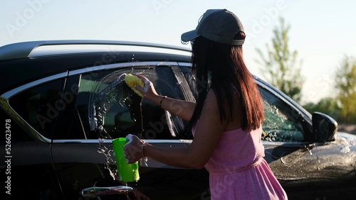 A young woman washes a car outside outdoors in the light of the setting sun. photo