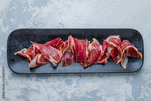 Spanish Jamon (Hamon), parma ham sliced on plate on white concrete table top view