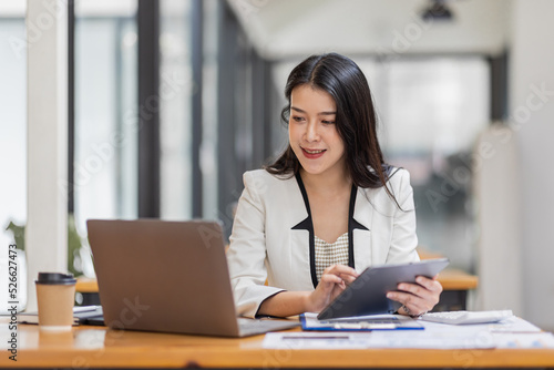 Female Business Asian working on documents on tablet laptop in the workplace, Young asian woman sitting at table doing planning financial report, business plan investment, finance analysis concept.