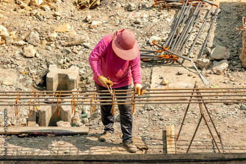 A construction worker equally spread out closed-loop steel bars along the length of deformed bars and ties them together with steel wires.