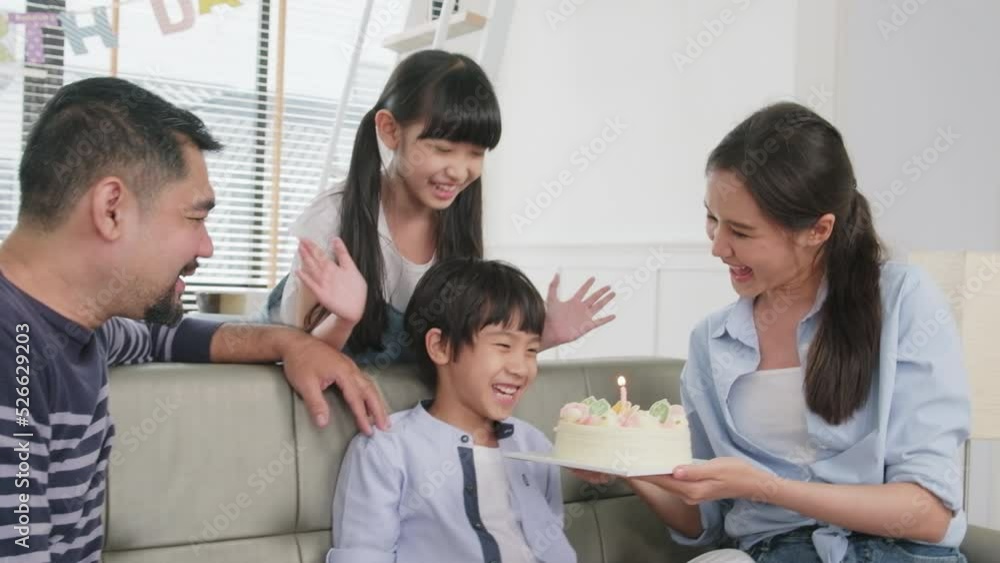 Happy Asian Thai family, young son is surprised with birthday cake, gift, blows out candle, and celebrates party with parents together in living room, wellbeing domestic home event lifestyle. Happy Asian Thai family, young son is surprised with birthday cake, gift, blows out candle, and celebrates party with parents together in living room, wellbeing domestic home event lifestyle.
