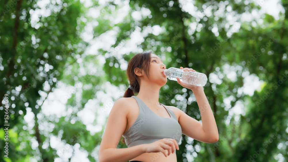 Young asian woman drinking water from a bottle while taking a break during her workout. Happy adolescence female working out in the park and taking rest a break to drink water Young asian woman drinking water from a bottle while taking a break during her workout. Happy adolescence female working out in the park and taking rest a break to drink water