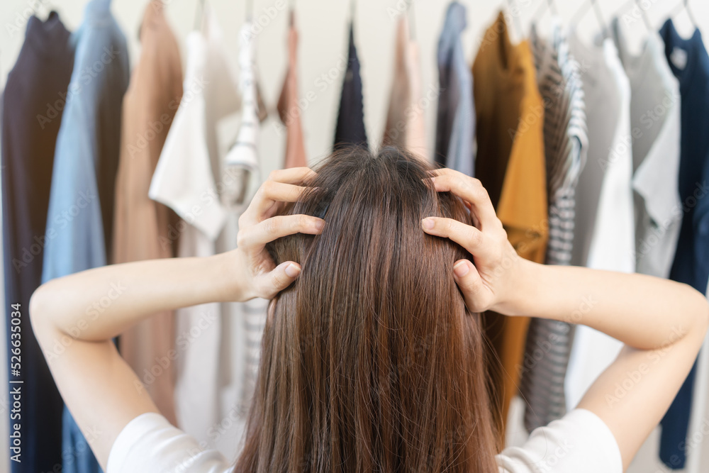 Naklejka premium Choice of clothes, Nothing to wear. Attractive asian young woman try on appare, stressed choosing dress, outfit on hanger in wardrobe in room closet at home. Deciding blouse what to put on which one.