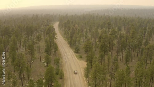 Smokey forest luxury SUV driving down dirt road. Aerial view follow footage of old scenic road in dense forest during smokey fire. Shot on 4k DJI Mavic 2 Pro.