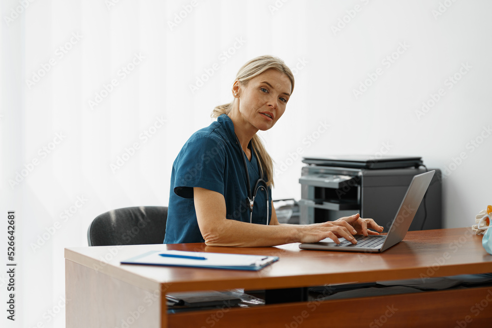 Female healthcare worker doing some paperwork and using laptop while working at doctor's office Female healthcare worker doing some paperwork and using laptop while working at doctor's office