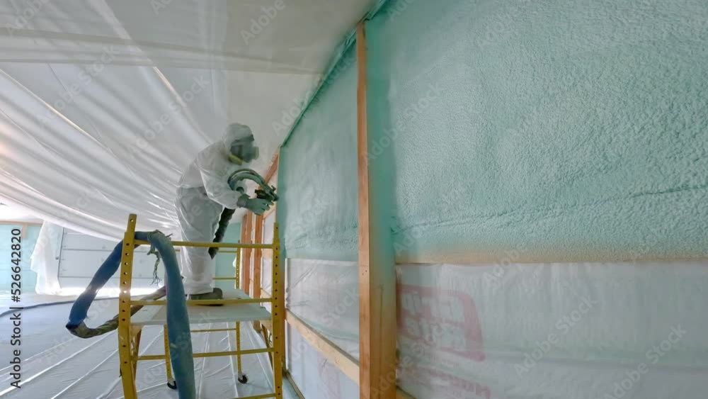 Man in respirator and Tyvek suit sprays closed cell foam insulation on