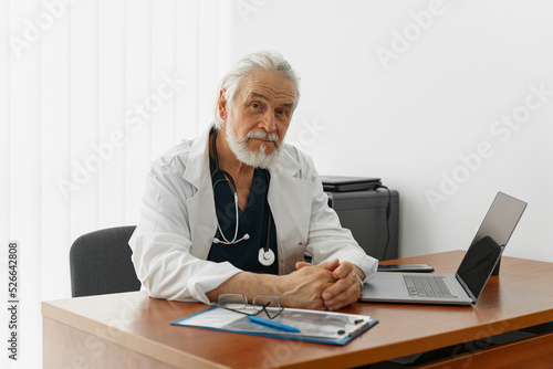 Senior healthcare worker doing some paperwork and using laptop while working at doctor's office