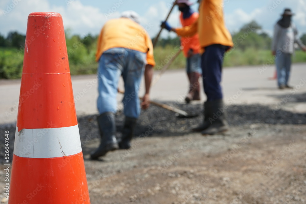Blurred image of road maintenance work in Asia and there is an orange cone in front.