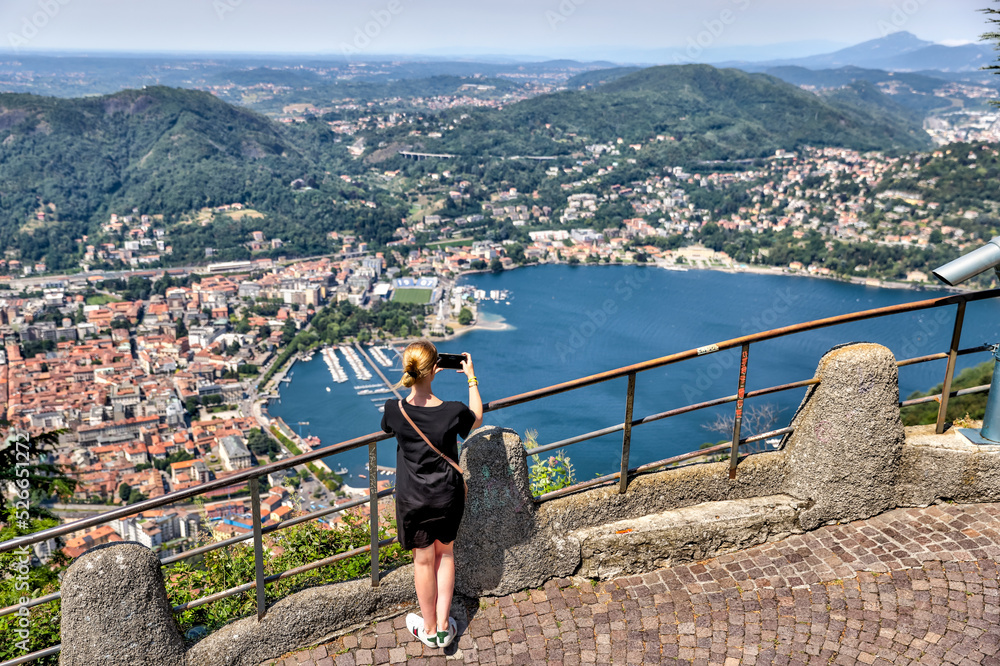 Young woman taking piactures of Lake Como from a mountaintop viewpoint
