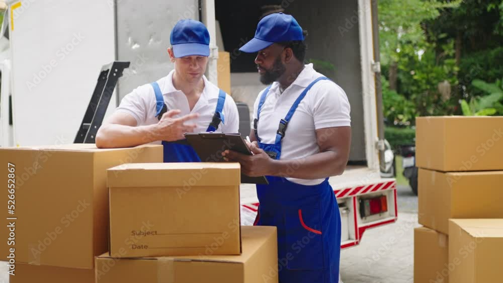 Workers unloading boxes from van outdoors.House move, mover service and Moving service concept.Two young handsome smiling workers wearing uniforms are unloading the van full of boxes. Workers unloading boxes from van outdoors.House move, mover service and Moving service concept.Two young handsome smiling workers wearing uniforms are unloading the van full of boxes.