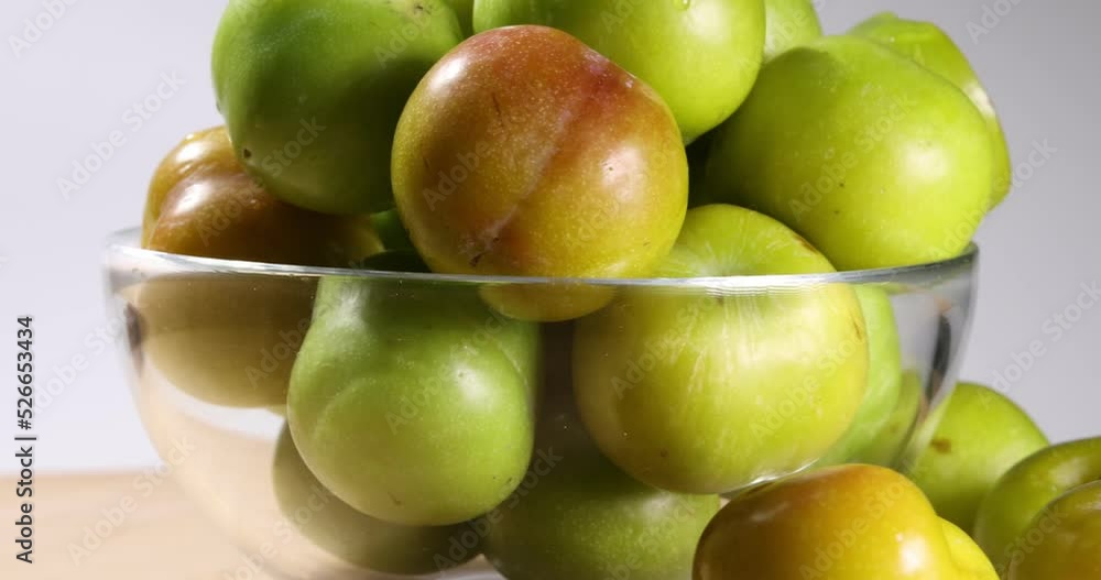 Small mini green fresh juicy plum fruit in transparent glass bowl wooden table white background turning rotating sliding Small mini green fresh juicy plum fruit in transparent glass bowl wooden table white background turning rotating sliding