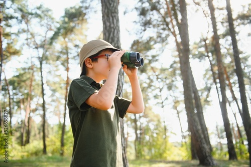 Little boy scout with binoculars during hiking in autumn forest. Concepts of adventure, scouting and hiking tourism for kids.