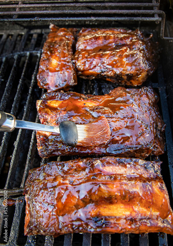 Foto Beef ribs being basted with bbq sauce on a grill with a basting brush