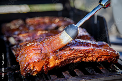 Beef ribs being basted with bbq sauce on a grill with a basting brush