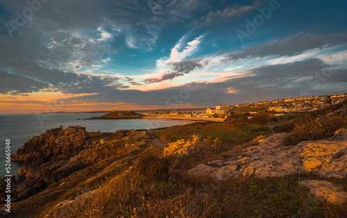 Fotografija Dramatic sunset in rugged coastal area; town appears in background