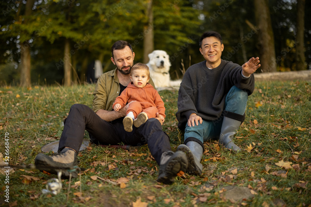 Fototapeta premium Multiracial male friends resting and fishing on river or lake coast. Concept of leisure and weekend in nature. Idea of friendship and enjoying time together. Caucasian man with little son. Autumn day