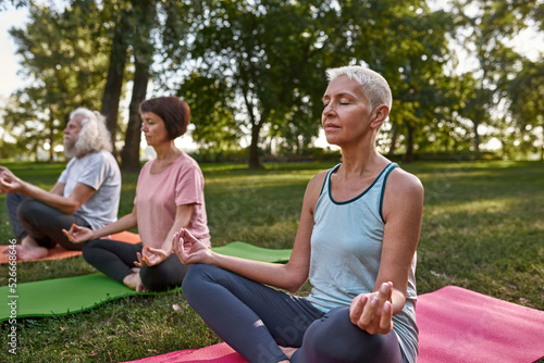 Woman with blurred friends practice yoga on meadow
